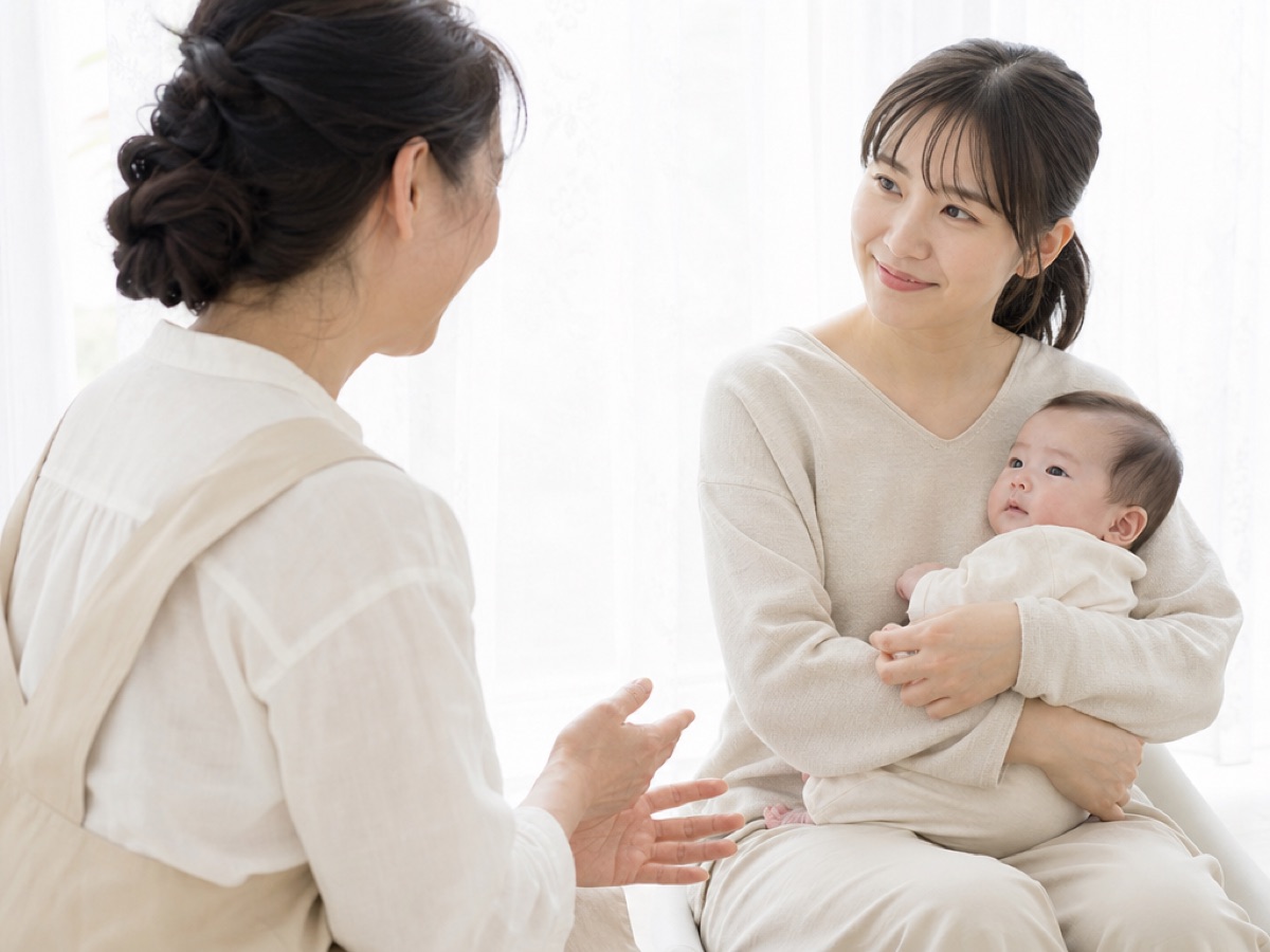 赤ちゃんを抱いた母親に、助産師が手ぶりを交えて話しかけている相談の様子
