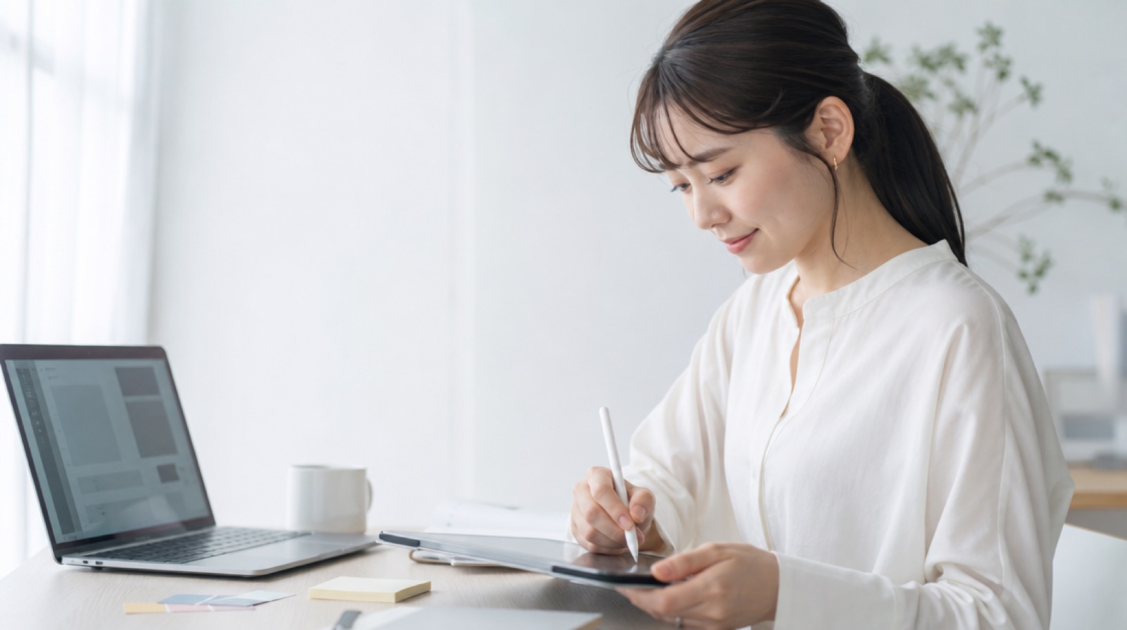 タブレットにペンでバナーのラフを描いている女性。机には色見本と付箋