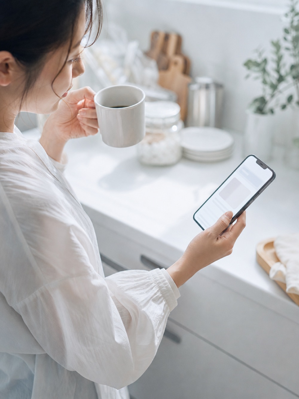 朝のキッチンでコーヒーを持ちながらスマートフォンを見る手元
